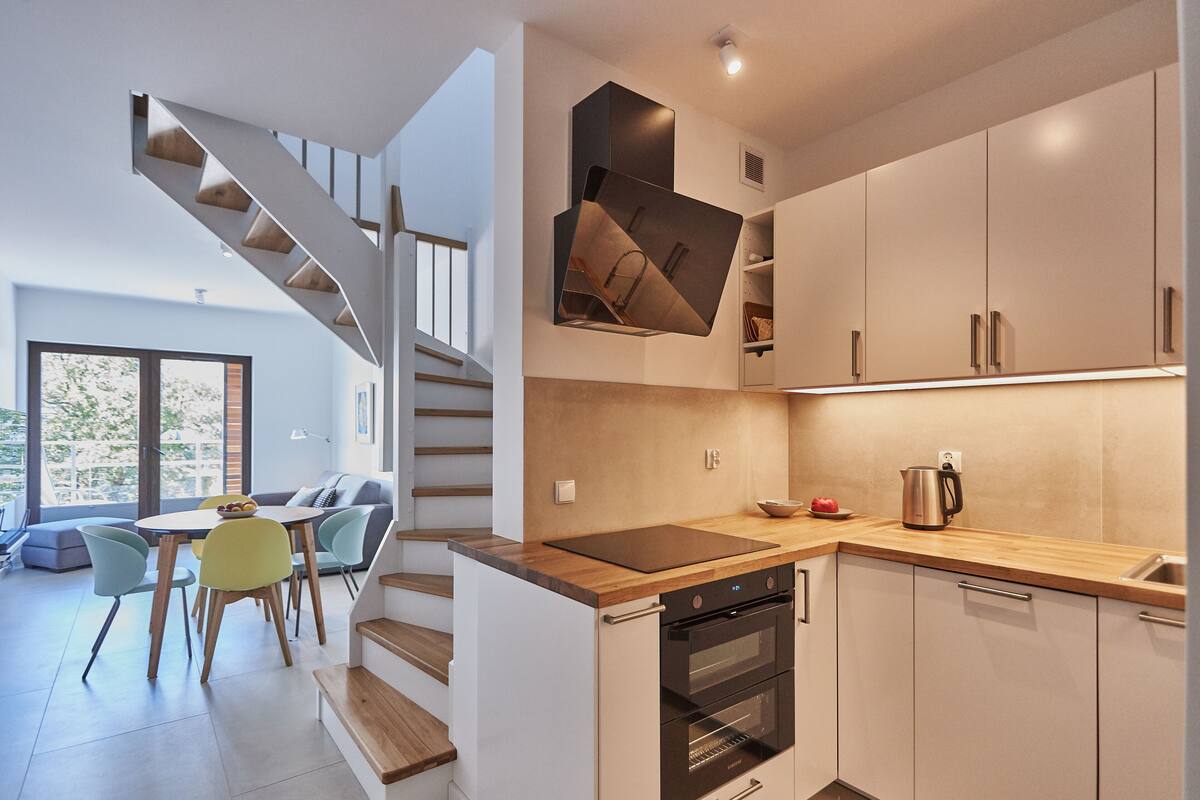 Una cocina moderna con horno empotrado, encimera de madera y comedor con mesa y sillas.