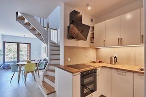 A modern kitchen with a built-in oven, a wooden countertop, and a dining area with a table and chairs. - Apartamenty Swinoujscie - Kormoran (Swinoujscie)