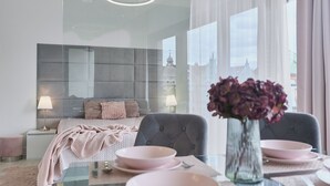 Une chambre à coucher moderne avec un lit, des tables de chevet, une table à manger en verre et un vase de fleurs.