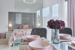 A modern bedroom with a bed, bedside tables, a glass dining table, and a vase of flowers. - Apartamenty Swinoujscie - Kormoran (Swinoujscie)