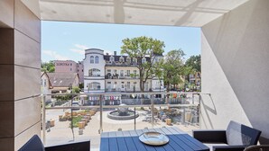 Un balcon avec une table et des chaises, donnant sur une cour intérieure agrémentée d’une fontaine et de bâtiments.