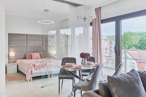A modern bedroom with a bed, bedside table, lamp, and a dining area with chairs and a table. - Apartamenty Swinoujscie - Kormoran (Swinoujscie)