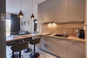 Cozinha moderna com bancada de madeira, duas luminárias pendentes, forno embutido e máquina de café.