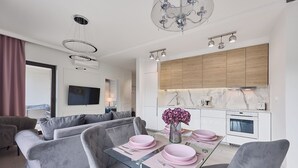 Una sala de estar moderna con una mesa de comedor de vidrio, sofás grises y una cocina con armarios de madera y encimera de mármol.