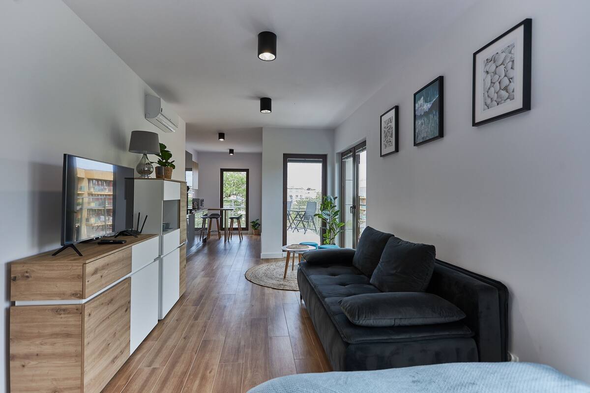 Un espacio habitable moderno con un mueble de madera, un sofá negro y un televisor sobre un soporte de madera.