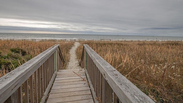 A wooden boardwalk leading to a beach with overcast skies. - The Captain's Quarters 2 Bedroom Home by RedAwning (Supply)
