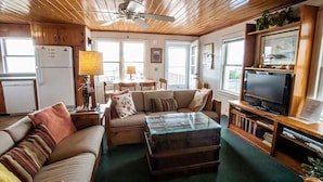 A cozy living room with a wooden ceiling, a glass coffee table, a sofa, a television, and a bookshelf. - The Captain's Quarters 2 Bedroom Home by RedAwning (Supply)