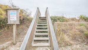 A wooden staircase leading up to a beach area with a signboard. - The Captain's Quarters 2 Bedroom Home by RedAwning (Supply)