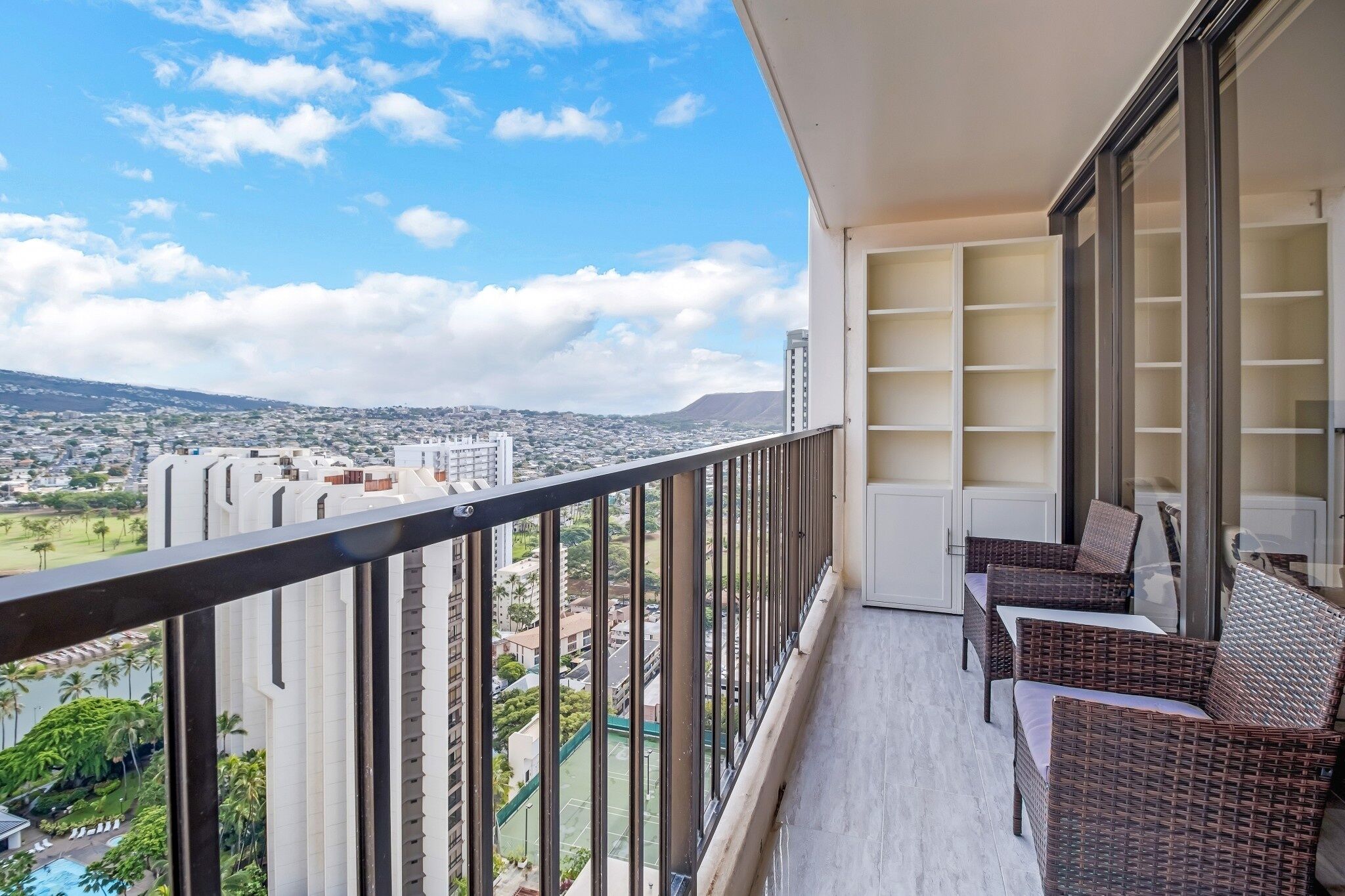 A balcony with wicker furniture, a view of a cityscape, and a clear sky.