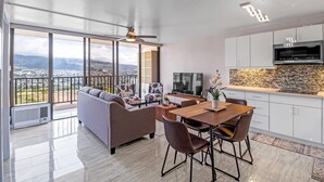 A modern living room with a sofa, chairs, a dining table, and a kitchen area with a TV and microwave.