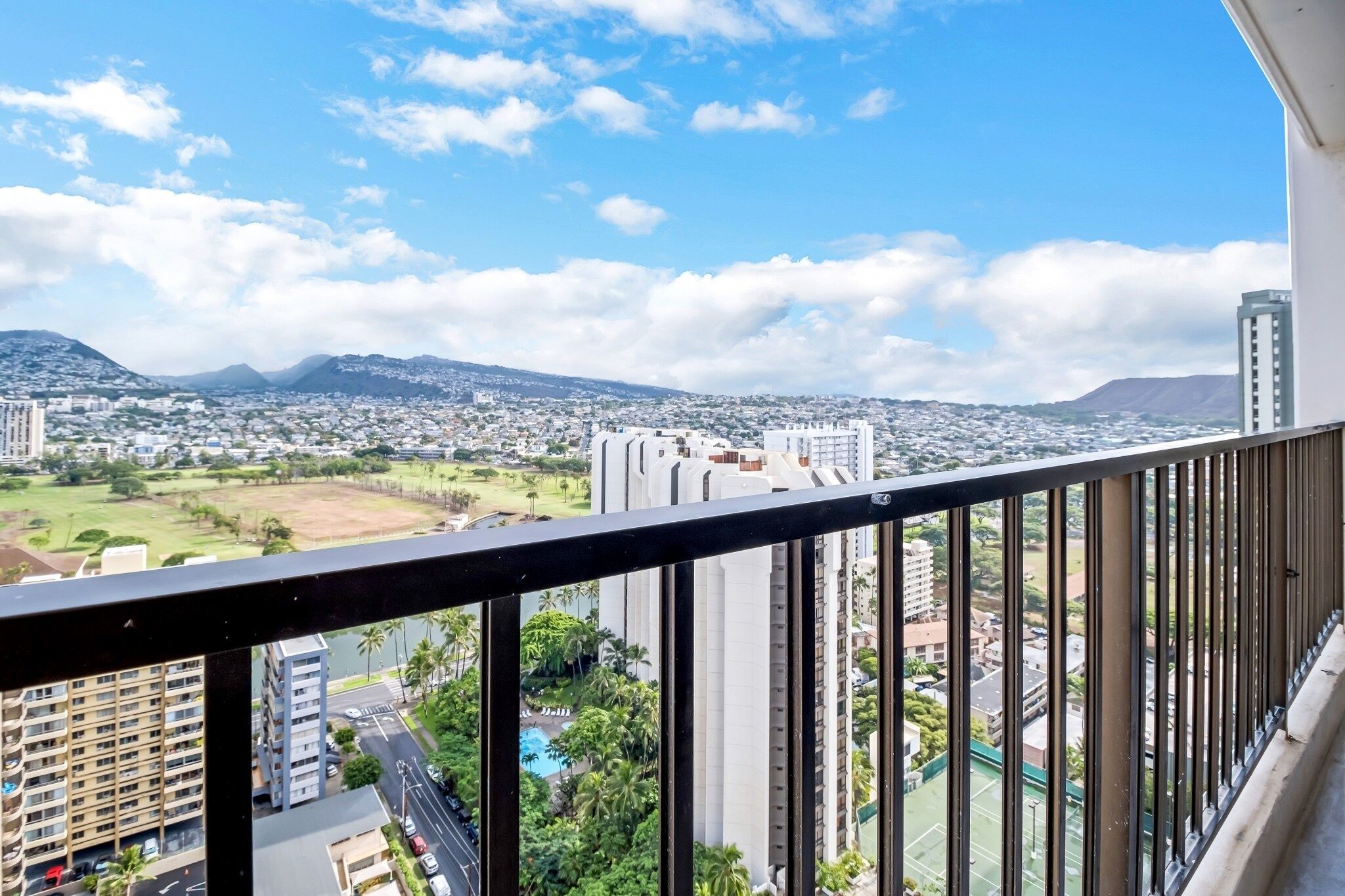 A balcony with a view of a cityscape, including high-rise buildings and a distant mountain range.
