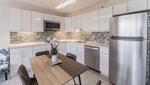 A modern kitchen with white cabinets, a stainless steel refrigerator, a microwave, and a brick backsplash.
