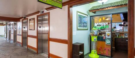 Un pasillo con ascensores, la entrada a una cafetería y una máquina expendedora.