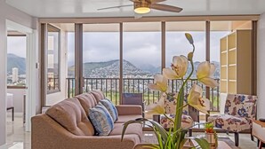 A spacious living room with a large sofa, a coffee table, and a chair, featuring a city view through large windows.