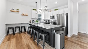 A modern kitchen with a central island, bar stools, stainless steel appliances, and pendant lighting.