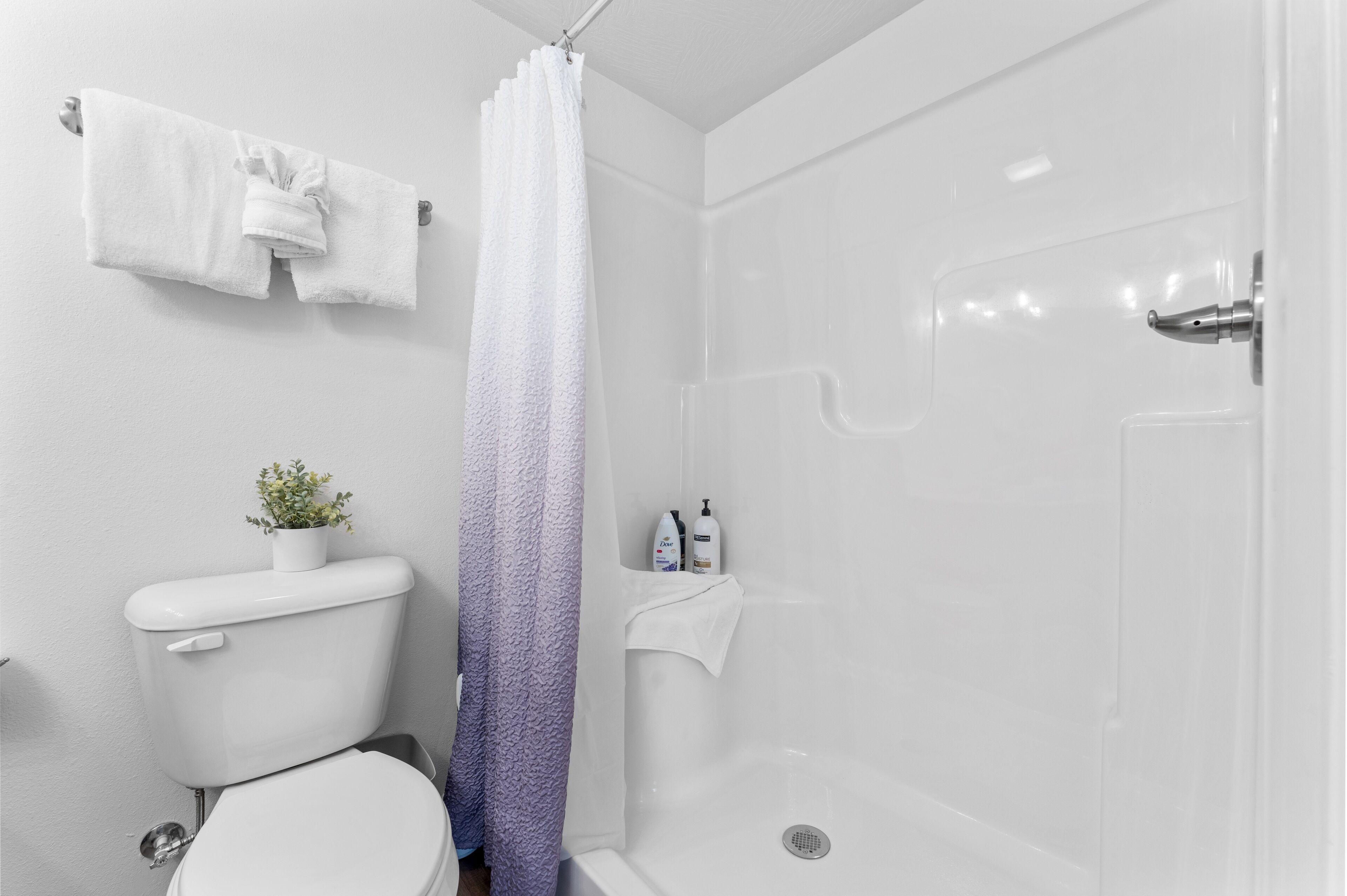 A bathroom with a toilet, a shower with a gradient curtain, and a towel rack with a towel.