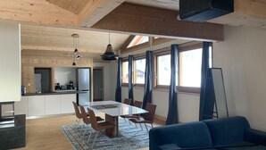 Uma sala ampla com uma mesa de jantar, sofá azul e cozinha ao fundo.