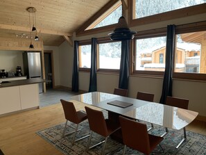 A modern kitchen with a refrigerator, coffee maker, and a dining area with a table and chairs.