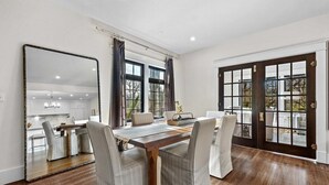 A dining area with a wooden table and four chairs, a large mirror, and a view through a glass door.