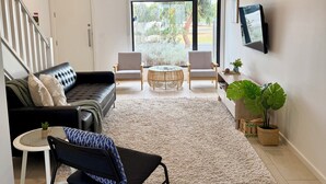 A modern living room with a sofa, chairs, a coffee table, and a TV mounted on the wall.