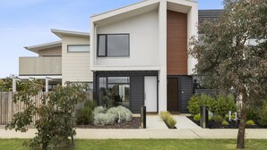 A modern two-story house with a flat roof, large windows, and a well-maintained garden.