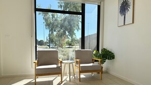 A room with two chairs, a small table, and a large window with a view of trees and a fence.