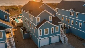 Uma área residencial costeira com várias casas azuis, uma garagem visível e vista para o oceano ao pôr do sol.