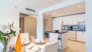 A modern kitchen with white cabinetry, a central island, and a dining area with white chairs and a table set for two.