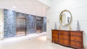 A lobby with two elevators, a wooden dresser with a mirror, and a tiled floor.