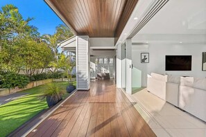 Un intérieur moderne avec un plafond en bois, un canapé blanc et une porte en verre donnant sur un balcon agrémenté de plantes.
