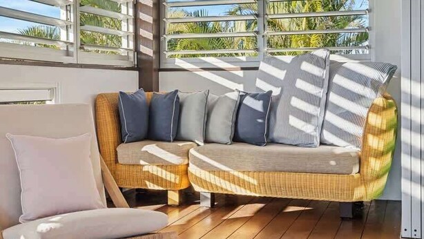 Un interior moderno con techo de madera, un sofá de mimbre con cojines y una silla blanca.