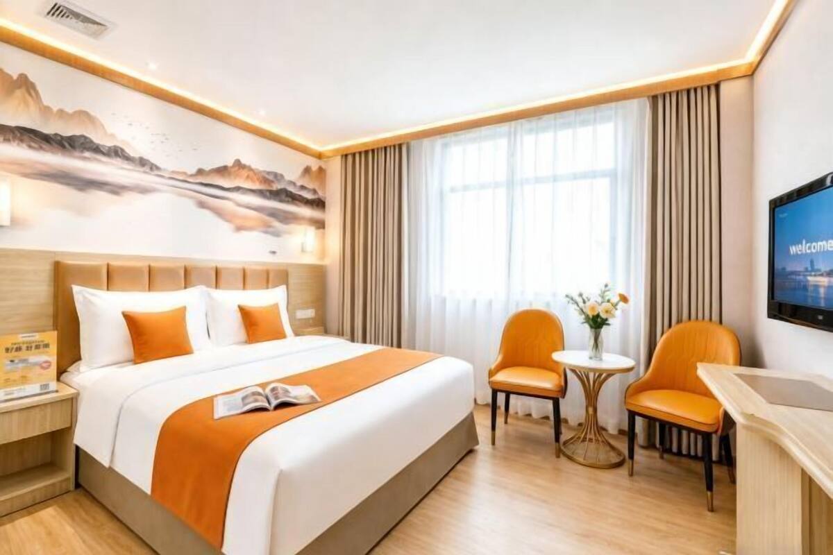 A hotel room with a bed, two chairs, a small table, a TV, and a painting on the wall.