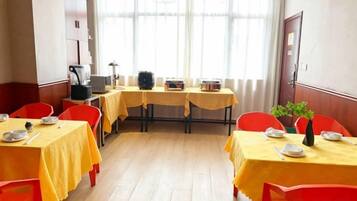 A dining area with tables set for four, chairs, and a window with curtains.