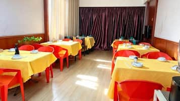 Un comedor con varias mesas y sillas dispuestas en filas, y una cortina al fondo.