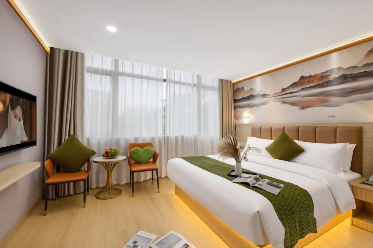 A hotel room with a bed, two chairs, a small table, and a painting on the wall.