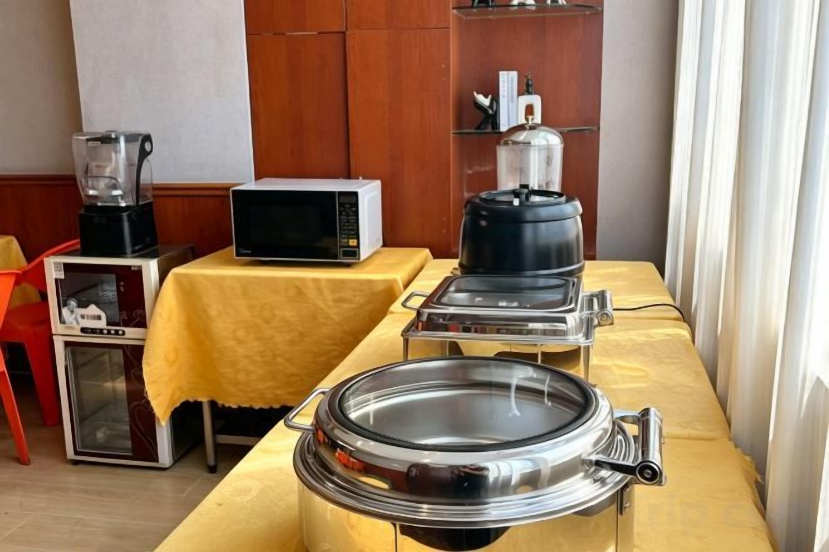 Disposição de buffet com micro-ondas, cafeteira e uma panela grande sobre uma mesa amarela.