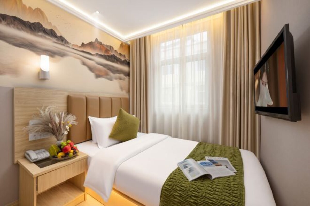 A hotel room with a bed, a nightstand, a wall-mounted TV, and a painting.