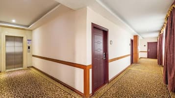 A hotel corridor with a patterned carpet, a wooden door, and an elevator.
