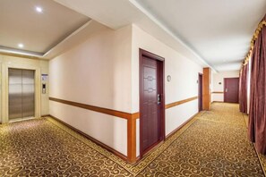 A hotel corridor with a patterned carpet, a wooden door, and an elevator. - Forbes Hotel (Shenzhen Longhua Dalang Commercial Center) (Shenzhen)