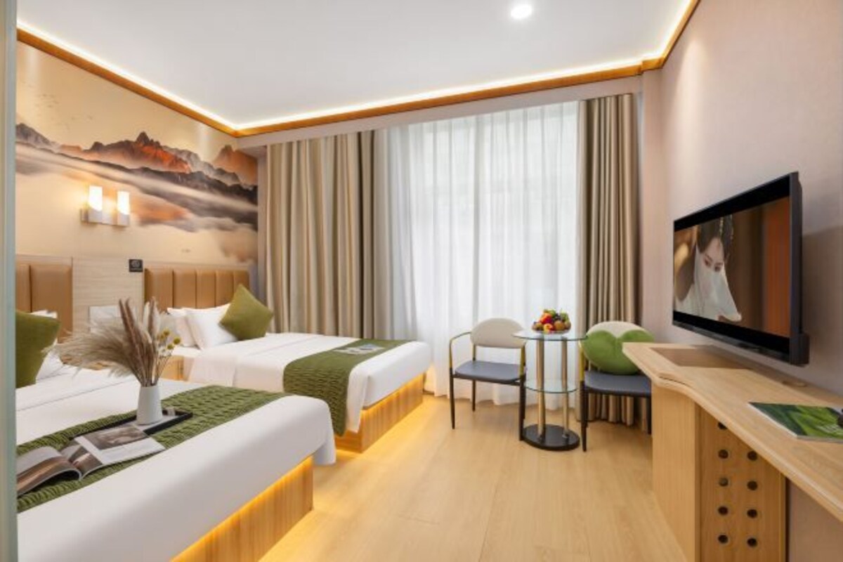 A hotel room with two beds, a TV, a small table with fruit, and a view of mountains.