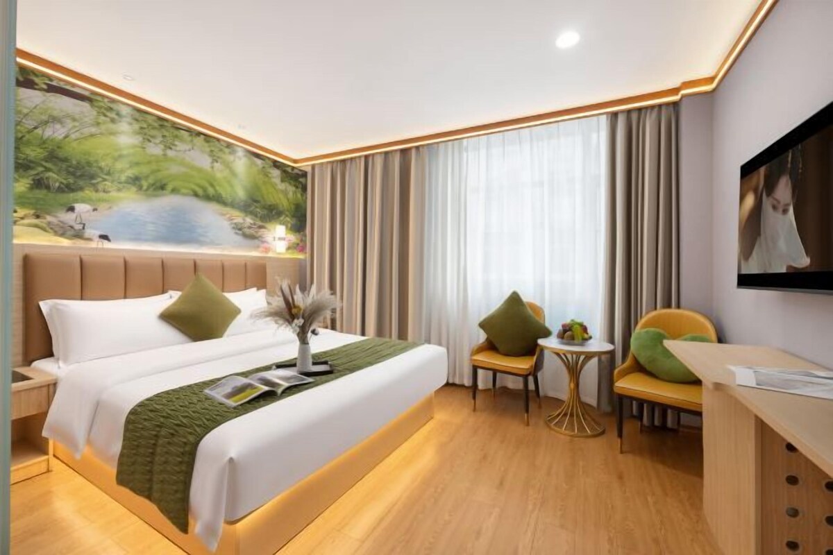 A hotel room with a large bed, a desk, a chair, and a television.
