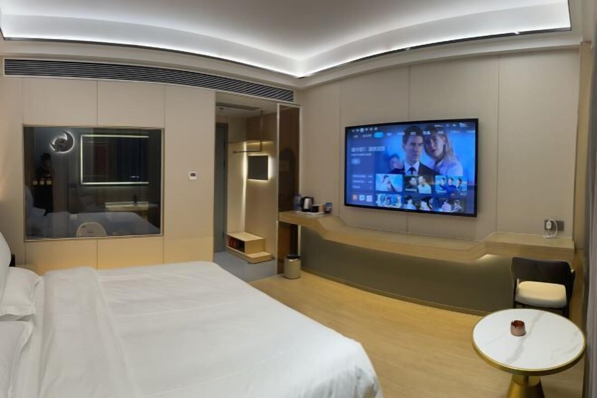A modern hotel room with a large bed, a TV mounted on the wall, a small table, and a seating area.