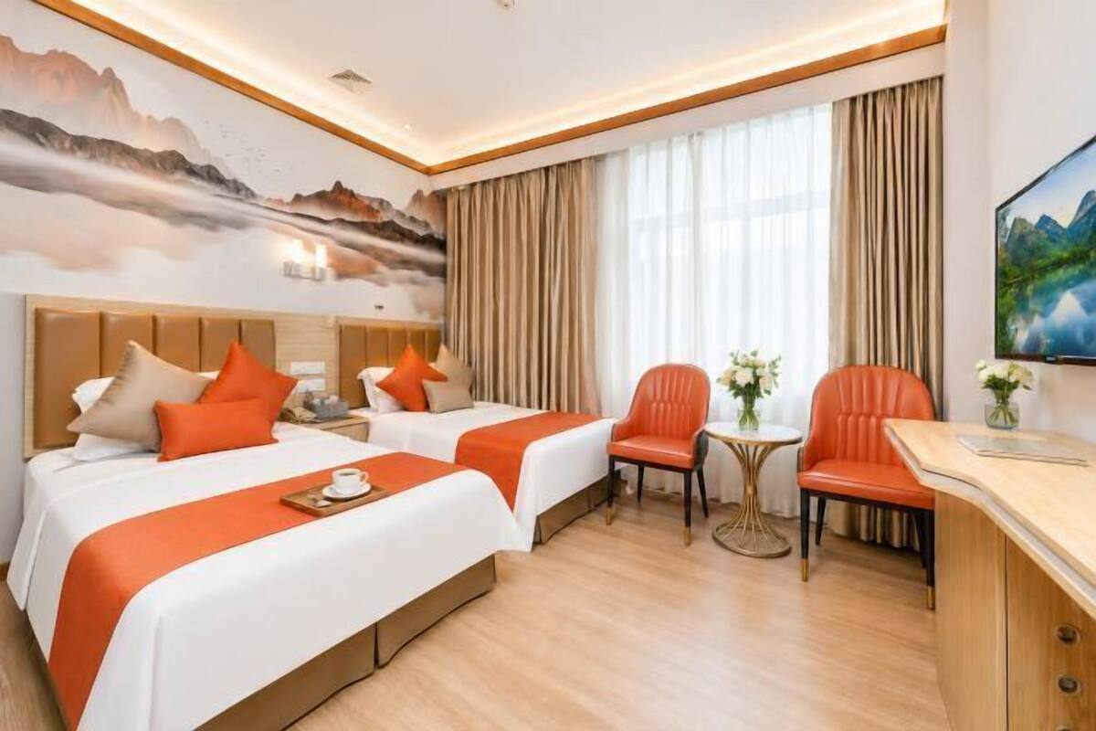 A hotel room with two beds, a desk, a chair, a small table, and a painting on the wall.