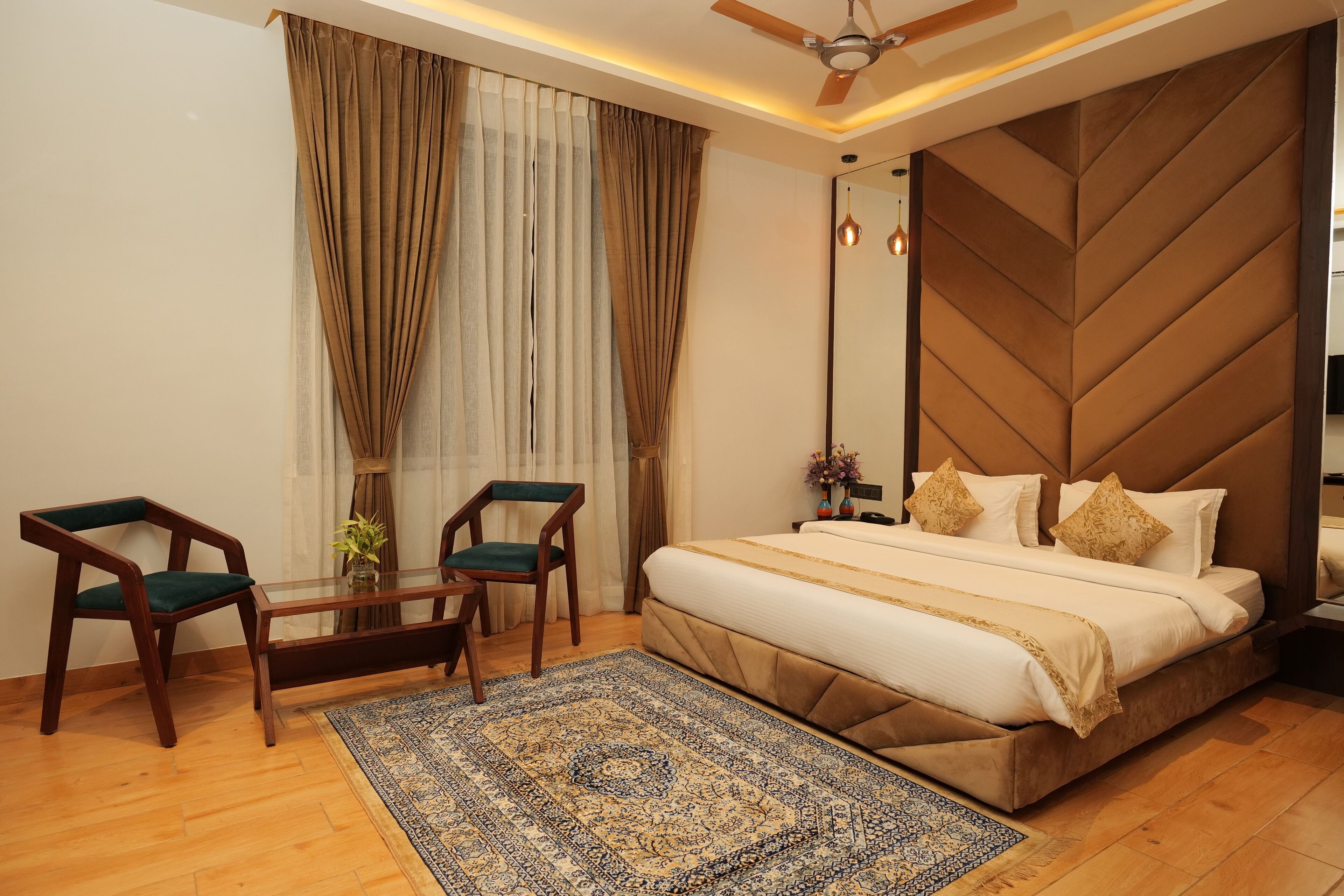 A bedroom with a large bed, a ceiling fan, a wooden headboard, and a small table with chairs.
