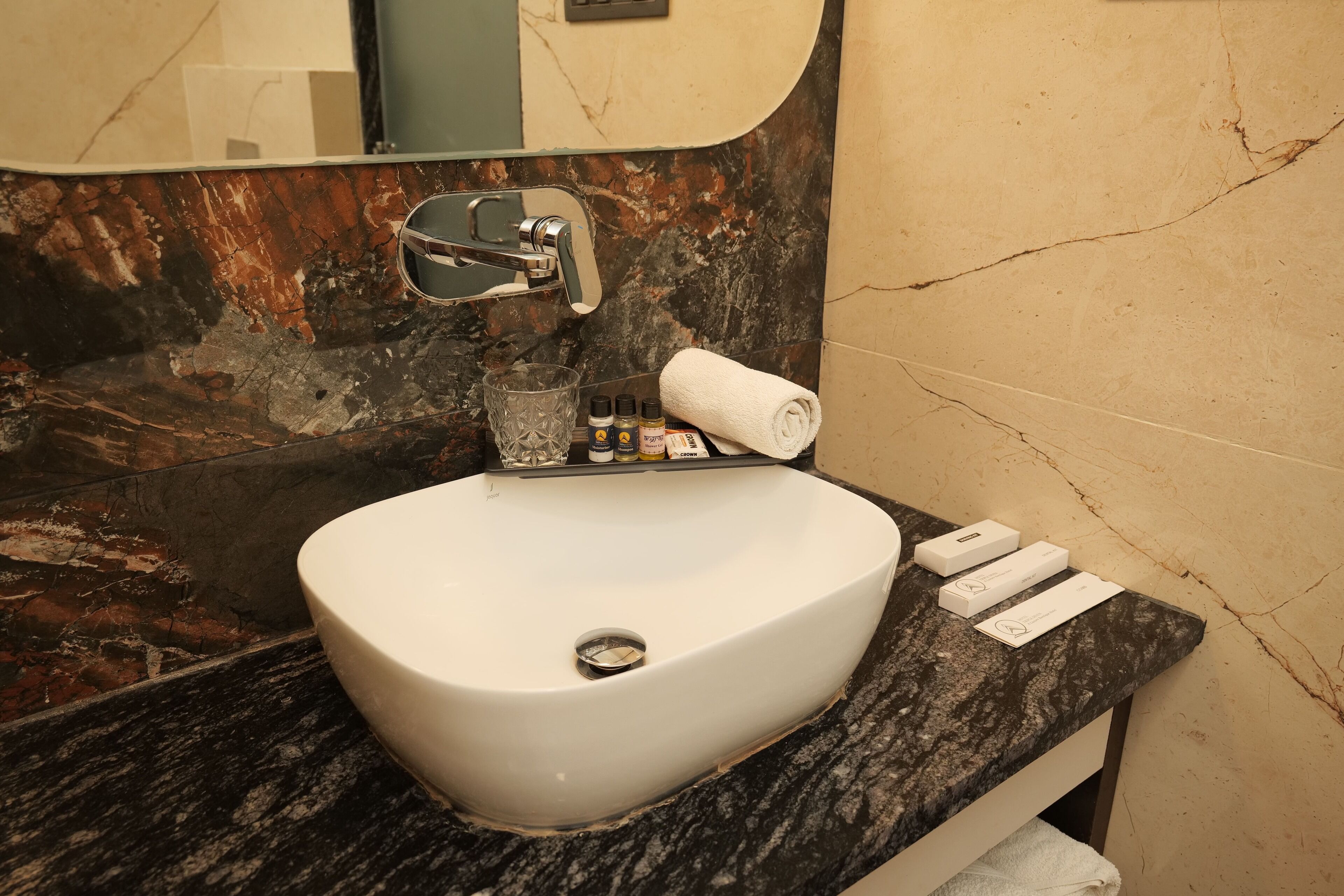 Un baño con un lavabo blanco, salpicadero de mármol, un espejo y artículos de aseo en la encimera.