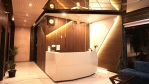A modern reception area with a wooden reception desk, a clock, and a ceiling fan. - Hotel 777, Pushkar (Pushkar)