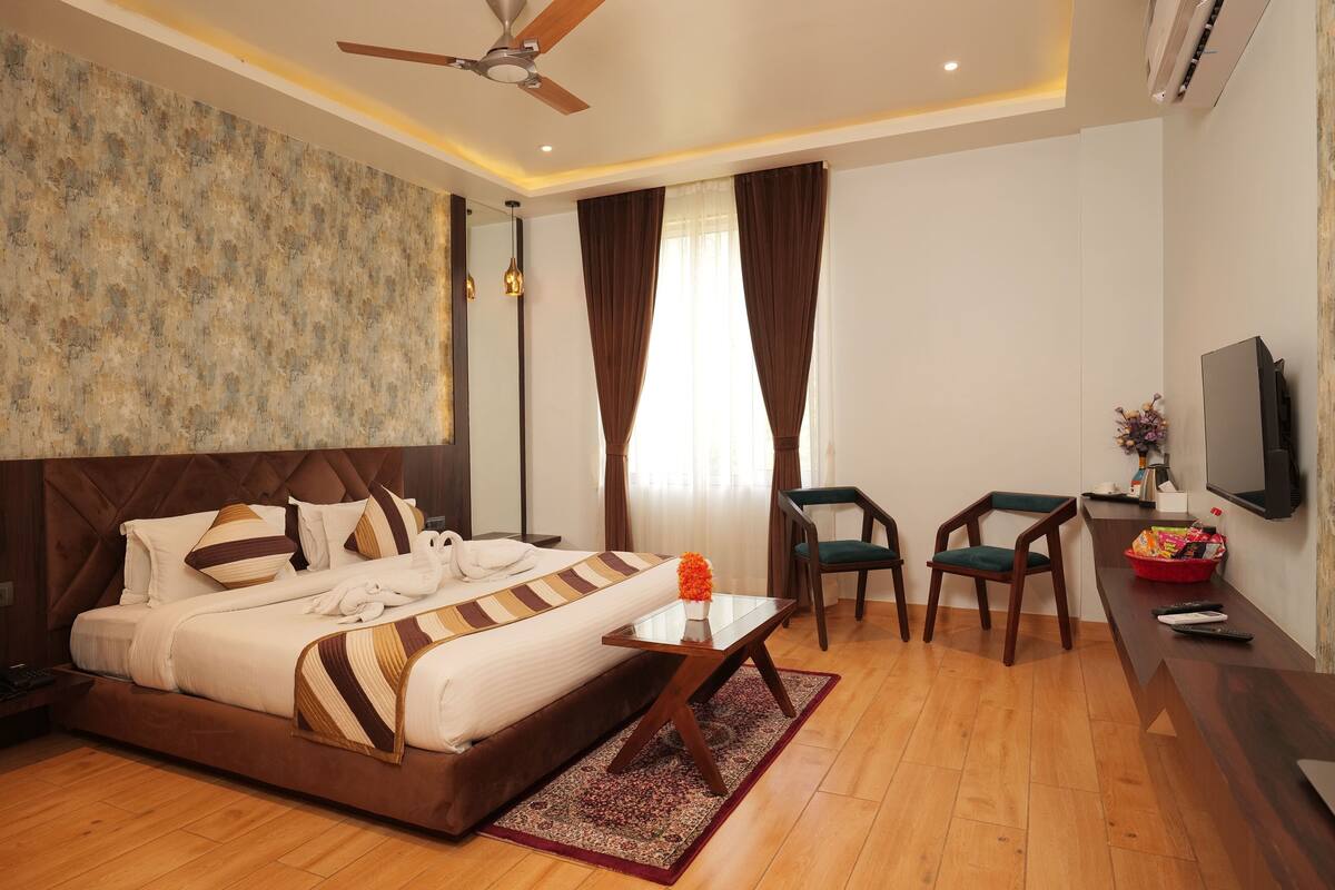 A hotel room with a large bed, a desk with a chair, a television, and a ceiling fan.