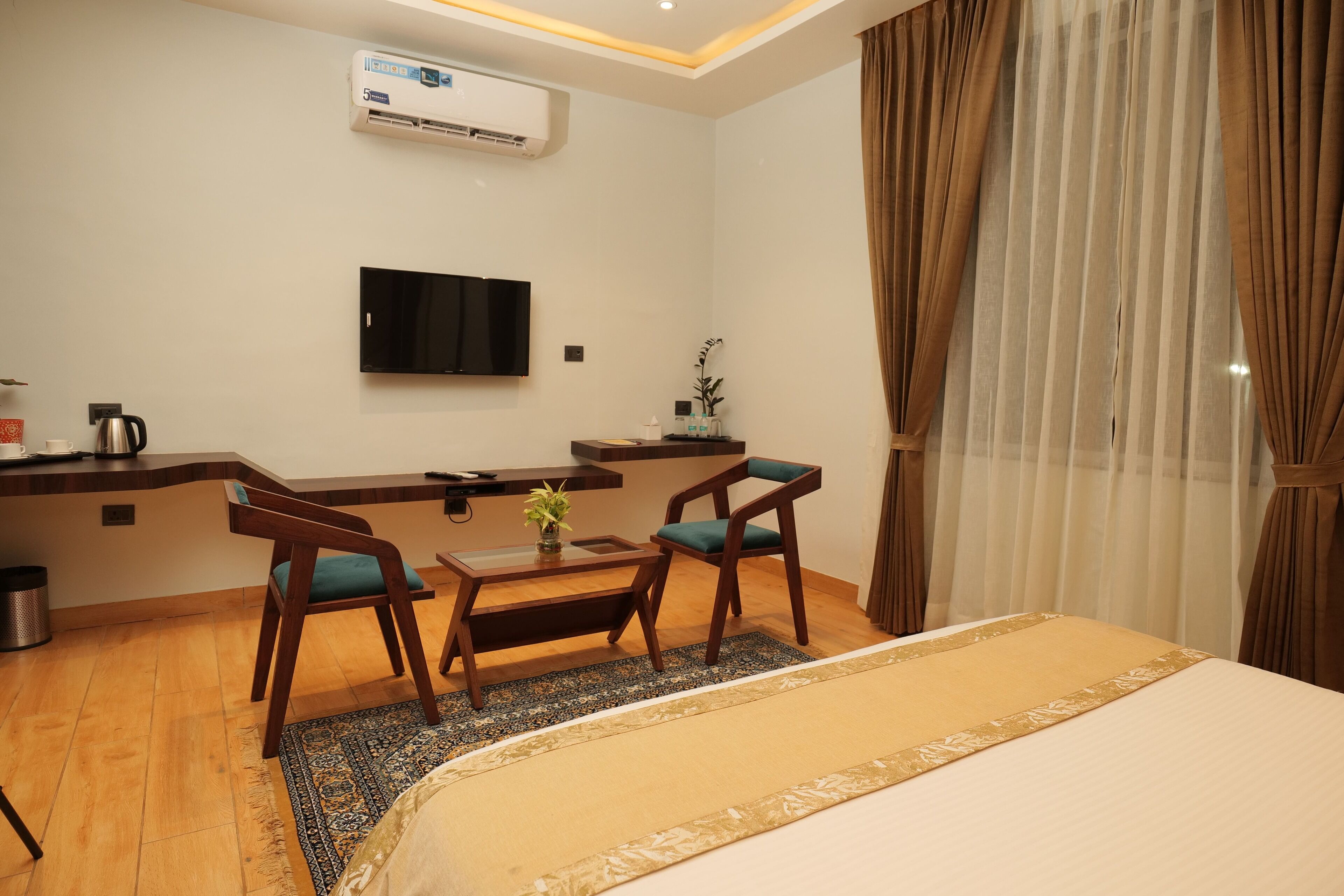A hotel room with a bed, a desk with a chair, a television, and an air conditioning unit.