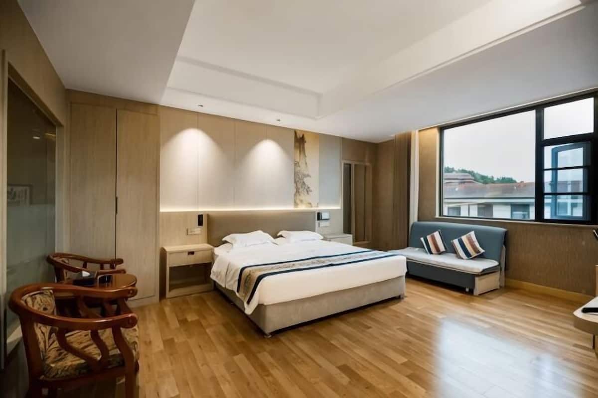 A modern hotel room with a large bed, a seating area with a sofa, a desk, and a chair.