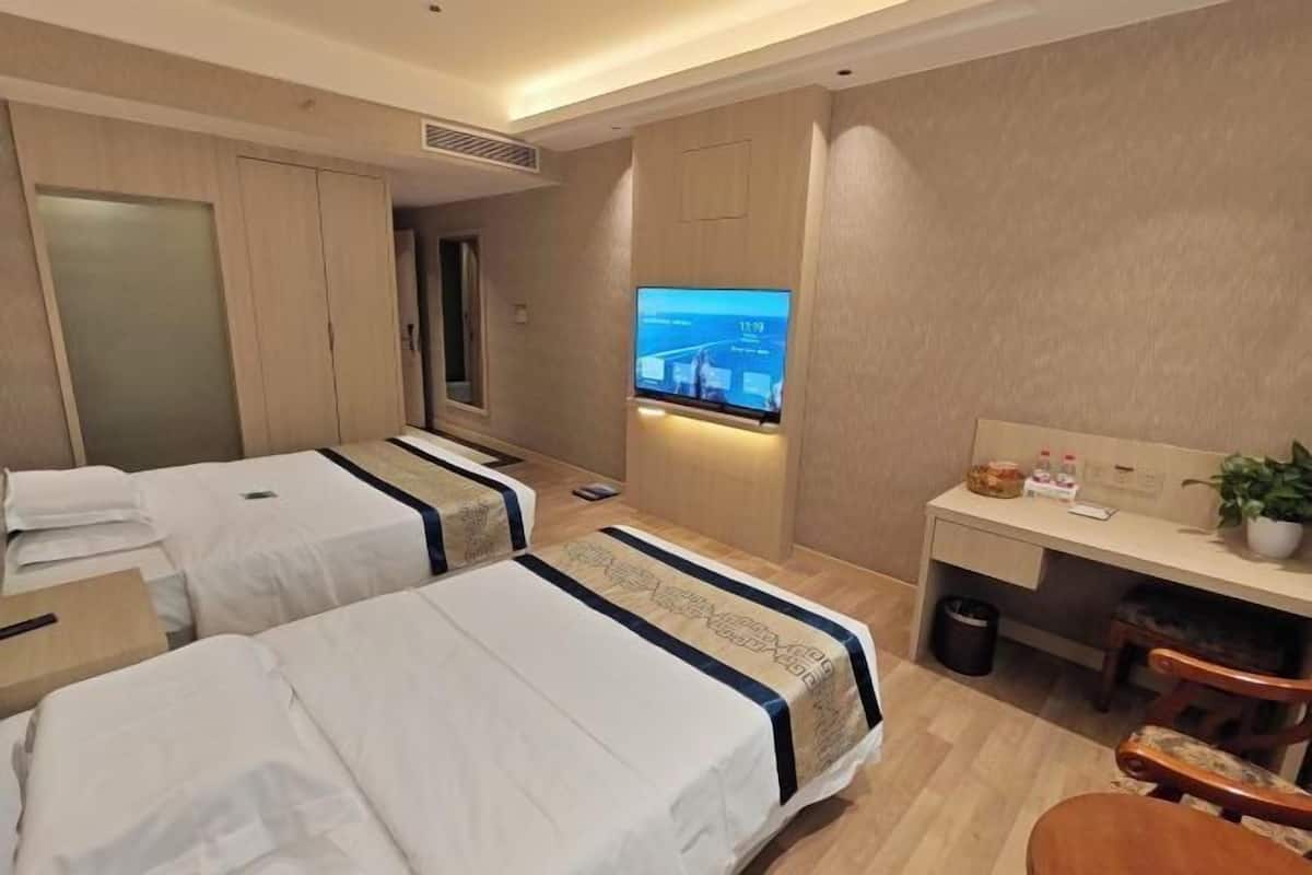 A hotel room with two beds, a desk, a TV, and a small seating area.
